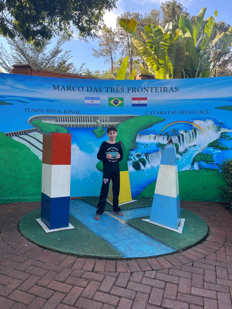 Diego no Marco das Três Fronteiras, entre colunas com as cores do Brasil, Argentina e Paraguai